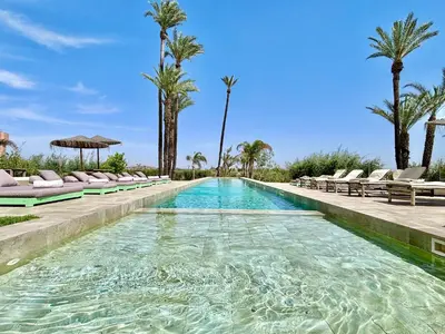 a swimming pool with chairs and palm trees at Palais Akbal in Marrakech