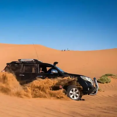 a black truck driving through the sand in the desert at Luxury Merzouga Desert Camp in Merzouga