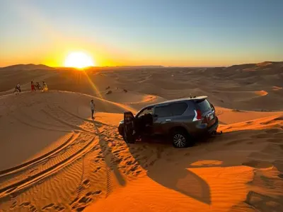 a suv parked in the desert at sunset at Awesome Luxury Camp in Merzouga
