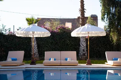 two lounge chairs and umbrellas next to a swimming pool at Palais Aureola Luxury Padel and Home Cinema in NʼChaba
