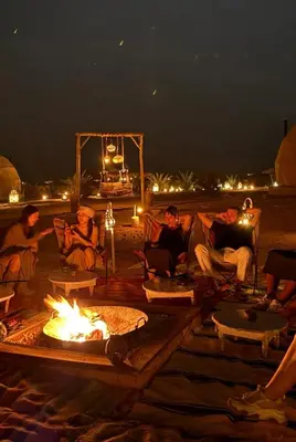 a group of people sitting around a fire pit at night at Serenity Sky Luxury Camp in Merzouga