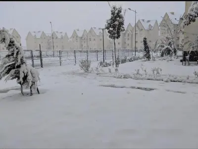 a yard covered in snow with a fence and houses at Casa De La Mama chauffée cosy et climatisée 3 pièces Ifrane sous la neige in Ifrane