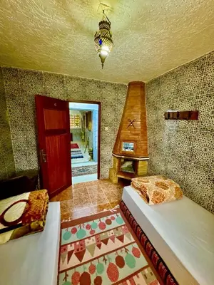 a bedroom with two beds and a fireplace in a room at Auberge Sous Les Étoiles Lac Ouiouane in Kasba des Aït Athmane