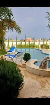 a large swimming pool with two chairs and a table at Villa Sarghini in Sidi Bouzguia