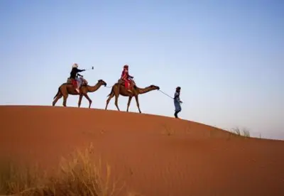 three people are riding on camels on a sand dune at Sands Charm Luxury Camp in Merzouga