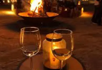 two glasses of wine sitting next to a fire pit at Sands Charm Luxury Camp in Merzouga