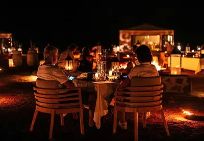 a group of people sitting at a table at night at Sands Charm Luxury Camp in Merzouga