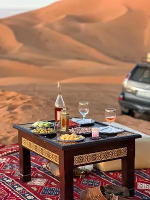 a table in the desert with food and wine at Merzouga Dunes Camp in Merzouga