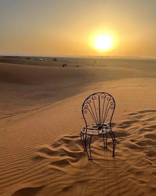 a chair in the desert with the sunset in the background at Merzouga Dunes Camp in Merzouga