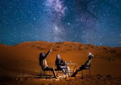 three people sitting at a table in the desert under the stars at Merzouga Dunes Camp in Merzouga