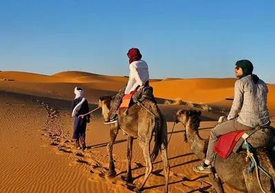 a group of people riding camels in the desert at Merzouga Dunes Camp in Merzouga