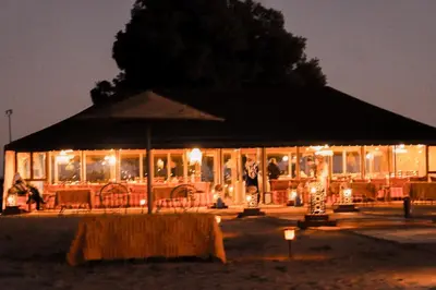 a building with an umbrella and tables and chairs at night at Paradise Luxury Camp in Merzouga