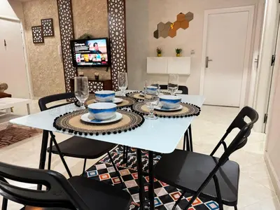 a dining room table with chairs and a white table with dishes on it at Appartement 2 Chambres à Hamria Meknès in Meknès