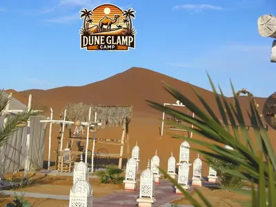 a desert scene with a dmg camel camp sign in front of a building at Dune Glamp Camp in Merzouga