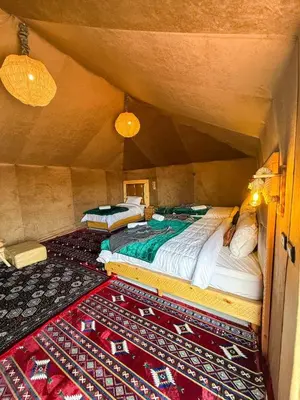 two beds sitting in a room with a rug at Dune Glamp Camp in Merzouga