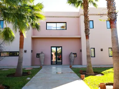 a pink building with palm trees in front of it at Villa des iris Domaines NAJMA in Marrakech