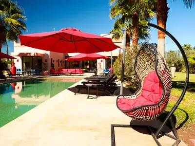 a chair with a red umbrella next to a pool at Villa des iris Domaines NAJMA in Marrakech