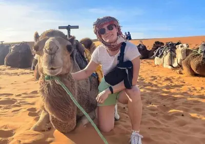 a woman is sitting on a camel in the desert at Sahara horizon Camp in Merzouga
