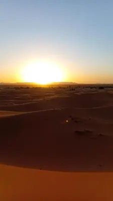 a sunset in the desert with the sun setting at Luxury Camp Sahara in Merzouga