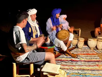 a group of men sitting around a table with a drum at Touareg spirit luxury Camp in Merzouga