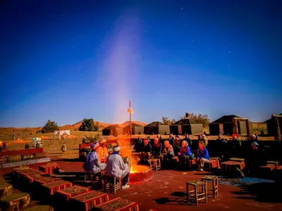 a group of people sitting around a fire in a stage at Incredible luxury Camp in Merzouga