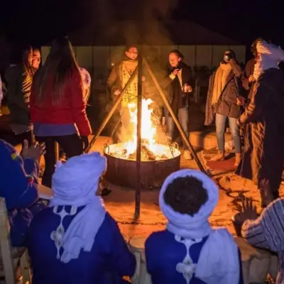 a group of people standing around a large fire at Sand Dunes Luxury Camp in Merzouga