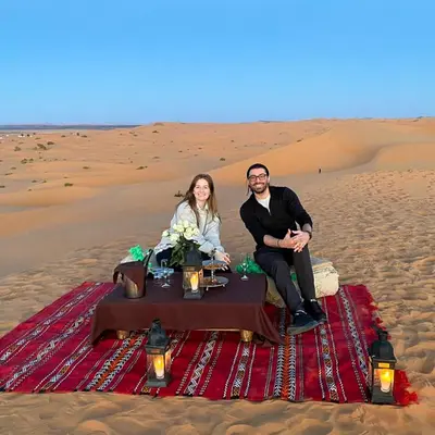 a man and woman sitting at a table in the desert at Sand Dunes Luxury Camp in Merzouga