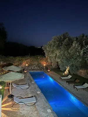 a swimming pool at night with chairs and umbrellas at Villa Hania 4 chambres avec piscine in Heddad