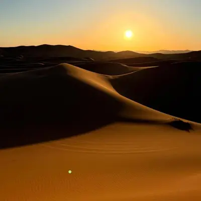 a desert sunset with the sun setting over the sand dunes at Merzouga Marvelous Camp in Merzouga