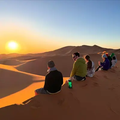 a group of people sitting in the desert watching the sunset at Merzouga Marvelous Camp in Merzouga