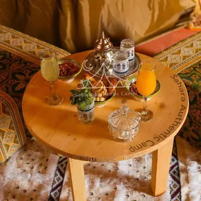 a wooden table with two glasses of orange juice at Sahara Authentic Camp in Merzouga