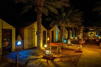 a resort with palm trees and lights at night at Sahara Garden Luxury Camp in Merzouga