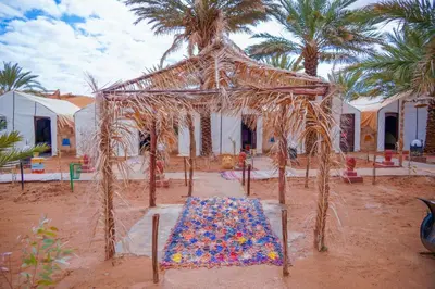 a tent with a table in the desert with palm trees at Sahara Garden Luxury Camp in Merzouga