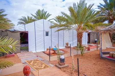 a large white tent in the desert with palm trees at Sahara Garden Luxury Camp in Merzouga