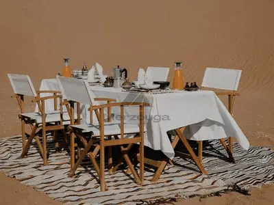 a dining table and chairs on the beach at Merzouga Luxurious Sahara Camps in Merzouga
