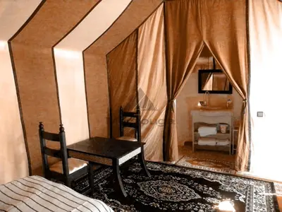 a bedroom with a bed and a chair and a table at Merzouga Luxurious Sahara Camps in Merzouga