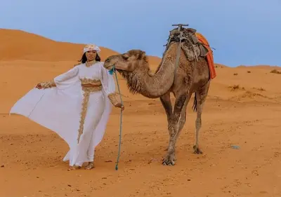 a woman standing next to a camel in the desert at Mystic Dunes Camp & desert activities in Merzouga