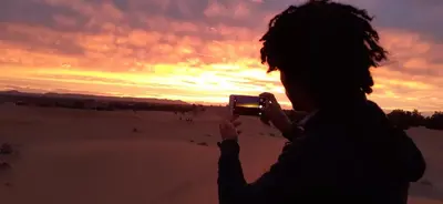 a woman taking a picture of the sunset with her cell phone at Sahara 4Seasons Appartement in Merzouga