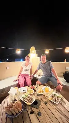 a man and woman sitting on a table with food at Riad Dar Sahara - Panoramic Rooftop in Nkob