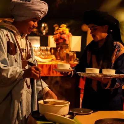 two people standing in a kitchen preparing food at Aurea Duna Luxury Camp in Merzouga