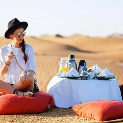 a woman sitting next to a table in the desert at Spectacular Luxury Camp in Merzouga