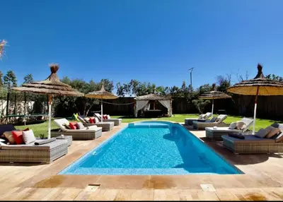 a pool with chairs and umbrellas in a yard at Sublime Villa Piscine & Jacuzzi in Marrakech