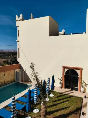 a white house with a swimming pool and blue umbrellas at Palm View Palace in Ouarzazate