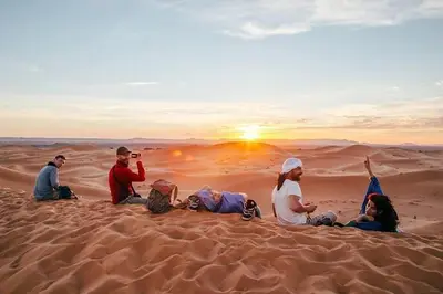 a group of people sitting on the sand in the desert at Merzouga Glossy Camp in Merzouga
