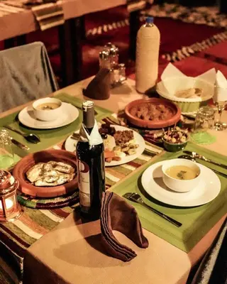 a table with plates of food and a bottle of wine at Merzouga Glossy Camp in Merzouga