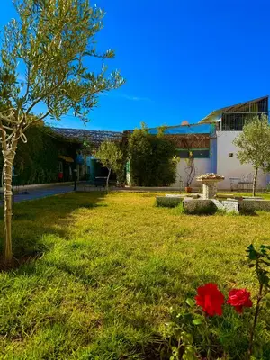 a green yard with a tree and red flowers at Hôtel Khalwa in Jenane Sidi Amer