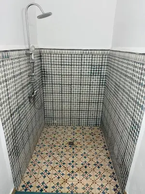 a bathroom with a shower with a tiled floor at Hôtel Khalwa in Jenane Sidi Amer