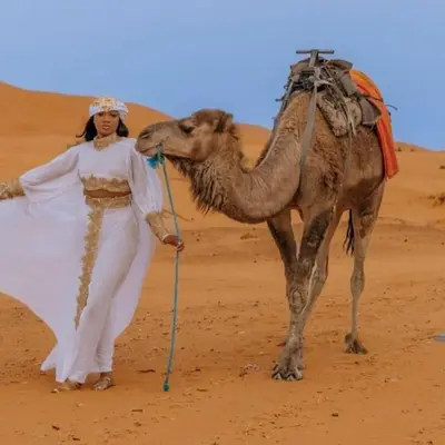 a woman standing next to a camel in the desert at Magnifique Luxury Camp in Merzouga