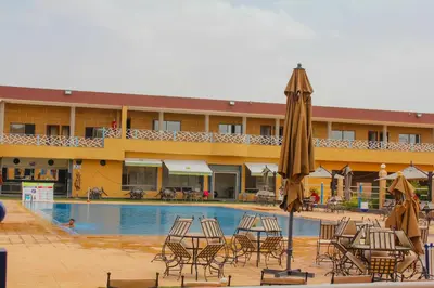 a hotel with a pool with chairs and an umbrella at Palmiers Hôtel Club in Er Rachidia