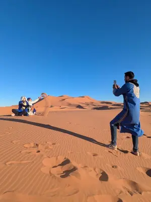 a woman standing in the desert taking a picture at Glamping Dunes Merzouga in Merzouga